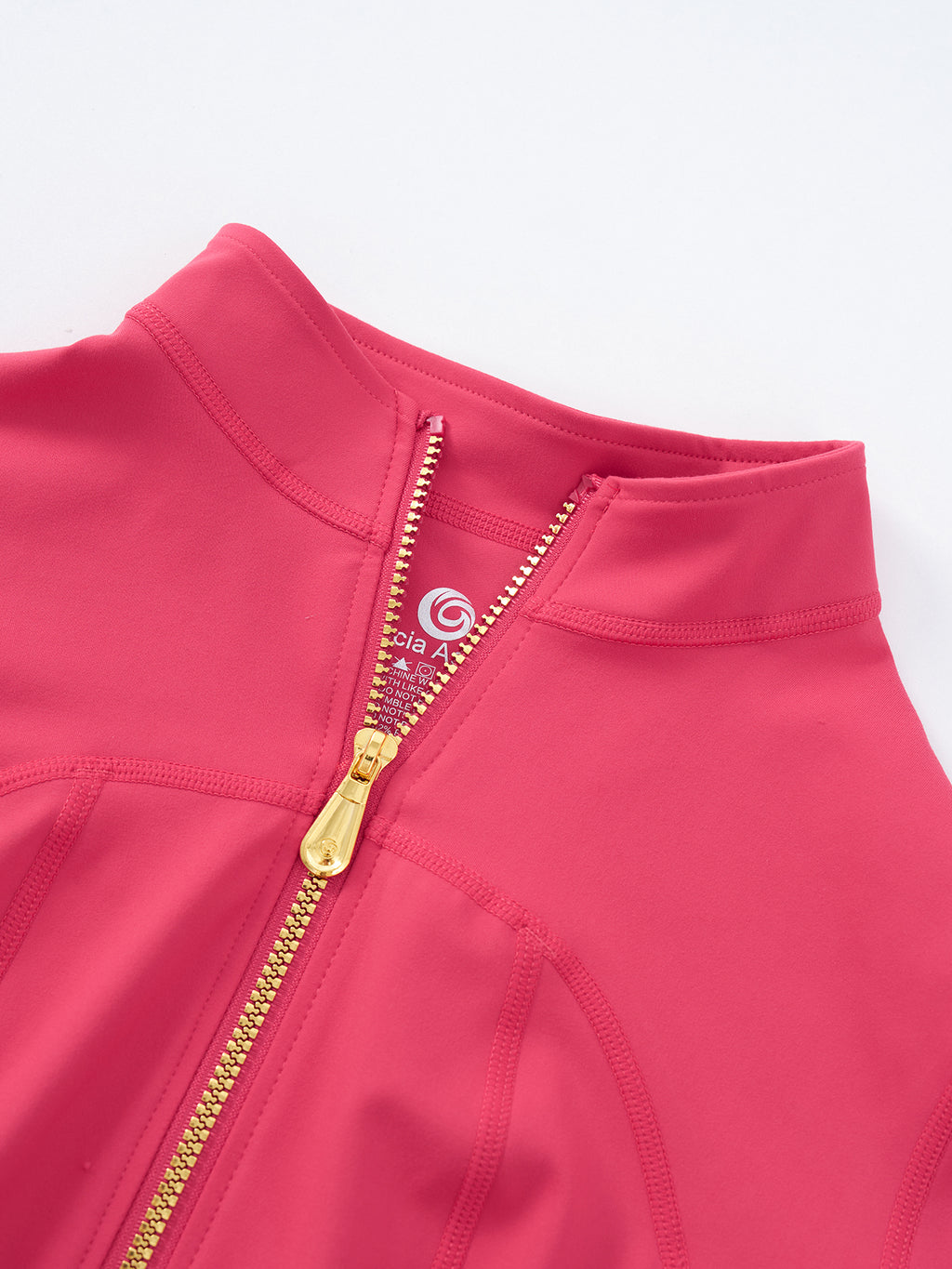 Close-up of a bright pink athletic zip-up jacket with a gold zipper and a visible circular logo on the inner neck label.