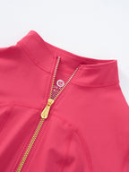 Close-up of a bright pink athletic zip-up jacket with a gold zipper and a visible circular logo on the inner neck label.