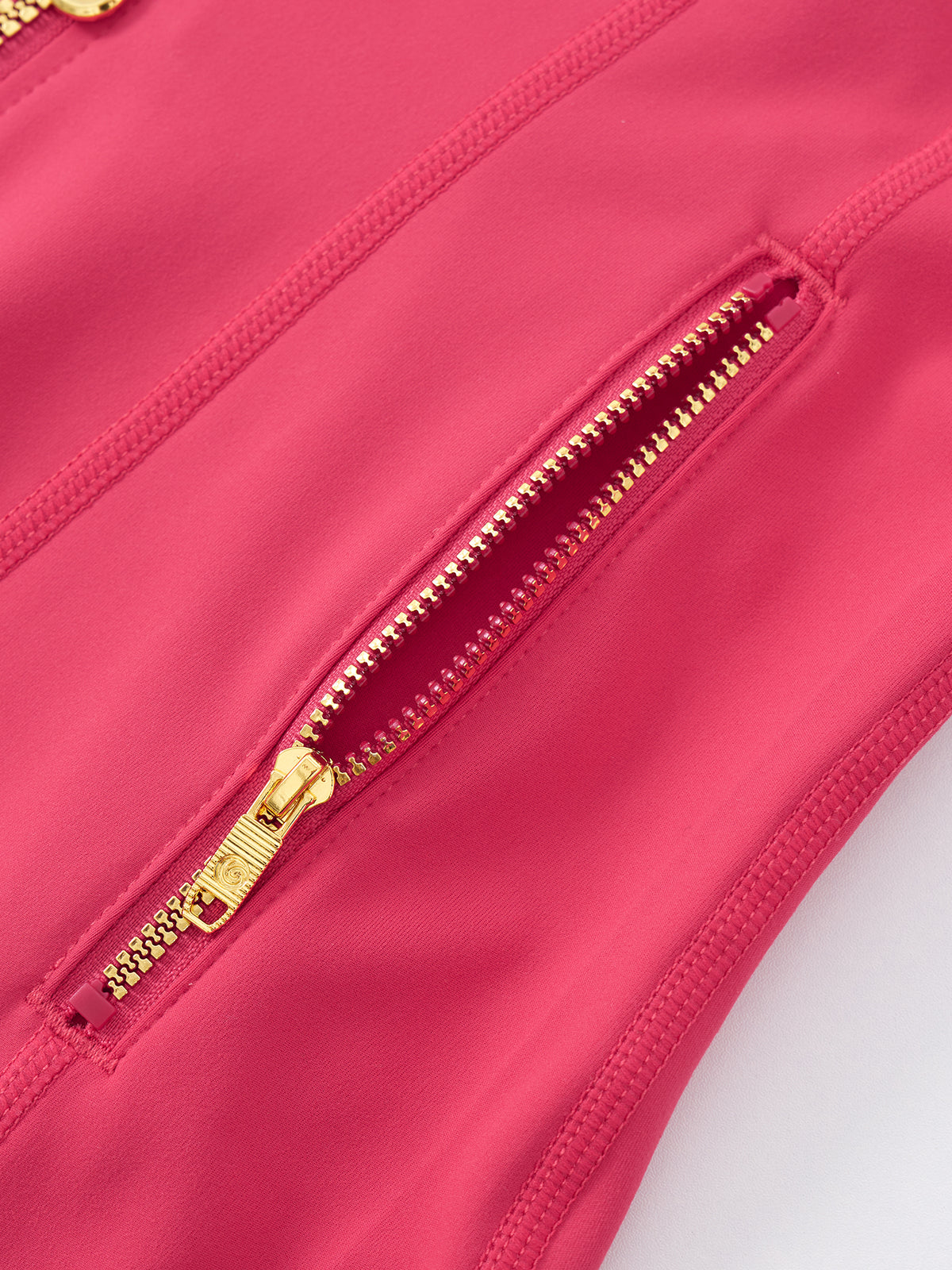 Close-up of a bright pink zippered garment detail with gold-tone zipper hardware on a white background.