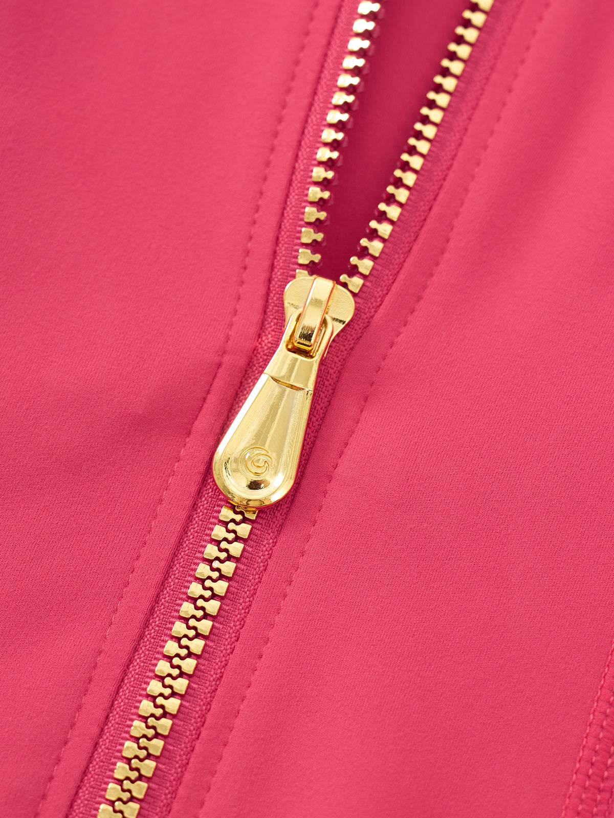 Close-up of a bright pink zippered garment with a shiny gold zipper pull and matching gold zipper teeth.